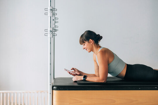 Woman Using Smartphone While Resting on Pilates Reformer Machine