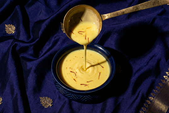 Pouring traditional Indian saffron sweet milk into a blue bowl