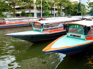 Obraz premium Public passenger boats running on canal in Bangkok city with buildings and trees on bank, water transportation and urban commuting travel.