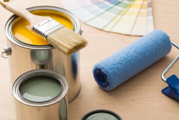 Naklejka premium Open cans of paint, brushes, roller, and color swatches on a light surface for renovation