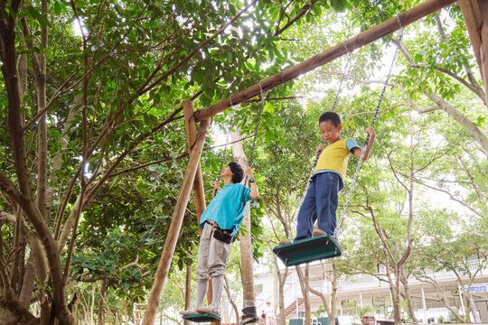Asian mother and son playing on a swing in the woods