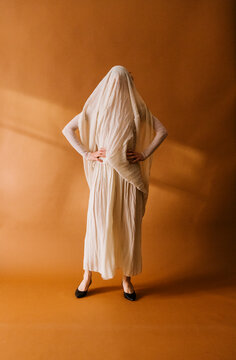 Mysterious Figure in Cream Dress Against Orange Backdrop