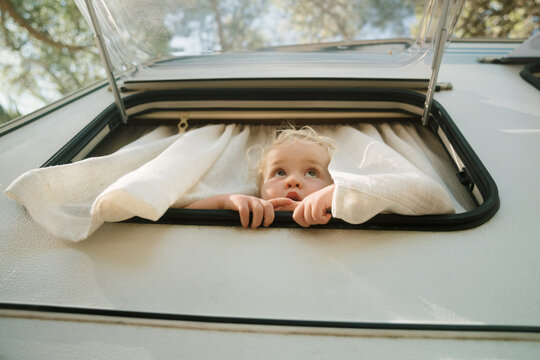 Child looks out of camper window during summer camping trip