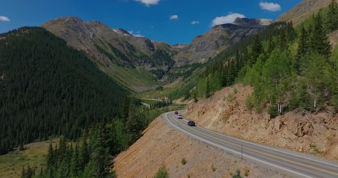 Remote mountain road sweeping by forested Colorado valley in bright daylight, Million Dollay Highway Colorado USA