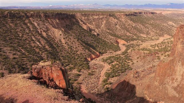 The drone camera exits the towering basalt walls of Diablo Canyon to reveal a winding sandy arroyo and sun-drenched plateau. This 4K shot captures the immense rugged scale of the New Mexico desert.