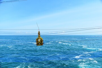 A gondola crossing a beautiful wavy blue sea with a blue sky. Timang Beach in Yogyakarta, Indonesia. © bachtiar.photography