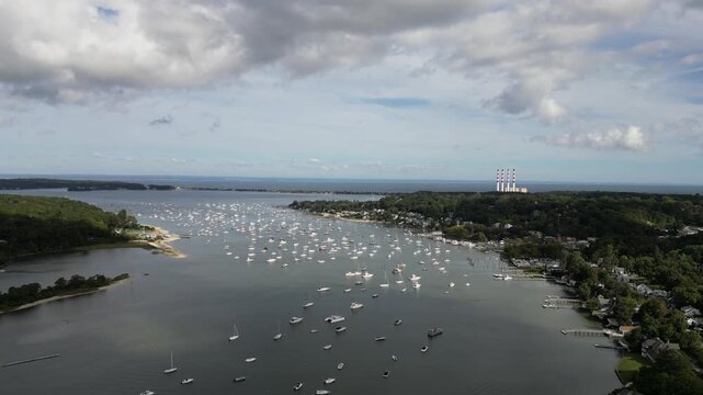 Beautiful aerial view of many sailboats and yachts anchored in the calm waters of port jefferson harbor in long island, new york, with a power plant visible on the horizon under a cloudy sky