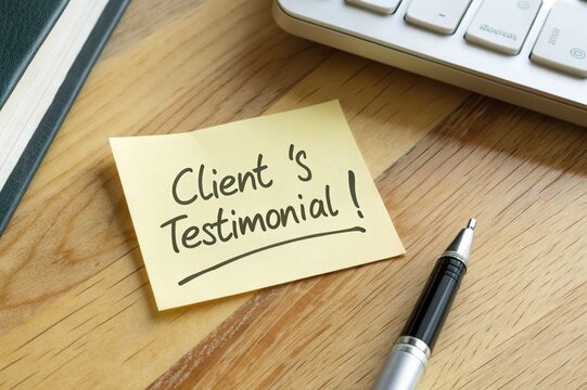 Sticky note with handwritten client testimonial on a wooden desk beside a pen and keyboard