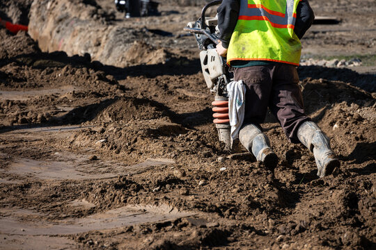 Construction worker using a compactor rammer machine to manually pack the fresh dirt covering trench a newly installed water pipeline, new municipal water distribution utility project work
