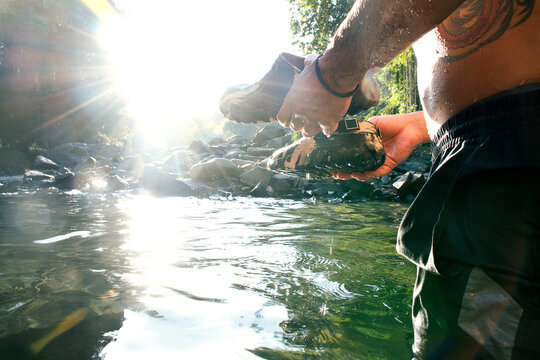 Man Washing Shoes in Clear River During Bright Sunny Day