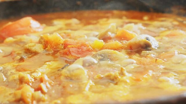 Vegetables simmer with chicken in a deep cast-iron skillet, simmering in a sauce and spices. Medium shot.
