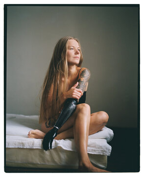 Woman with prosthetic arm sits on a bed in calm indoor setting