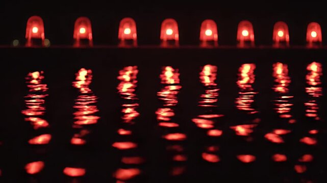 Row Of Red Warning Siren Lights Reflected Across Dark Rippling Water At Night