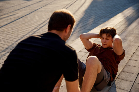Trainer supporting client during sit-up exercise outdoors