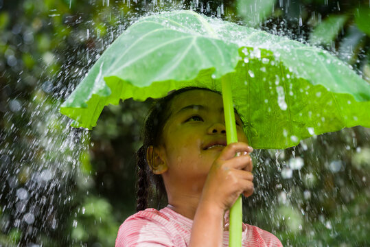 Girl smiling under large leaf sheltering from summer rain