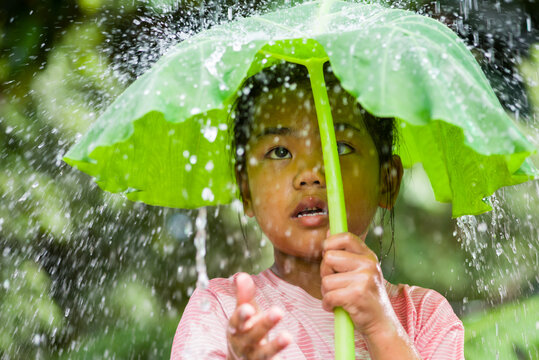 Girl smiling under large leaf sheltering from summer rain