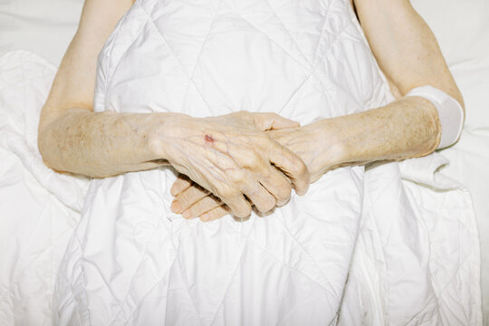 Elderly Hands Resting Gently Under a White Blanket on a Bed