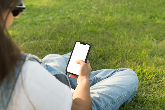 Person using smartphone while sitting on grass in sunny park