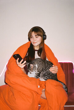 Cozy Moment: Woman with Cat in Orange Blanket Listen To Music
