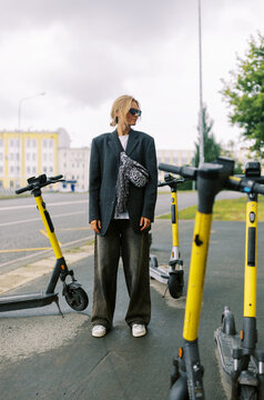 Stylish Person Stands Near Electric Scooters in Urban Setting