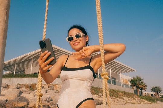 Smiling woman taking a selfie on a swing at the beach on a sunny day
