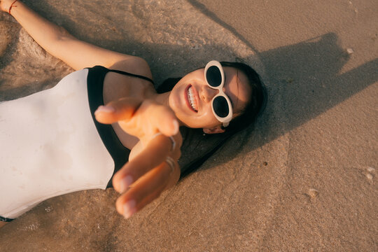 Woman lying on the beach reaching toward the camera
