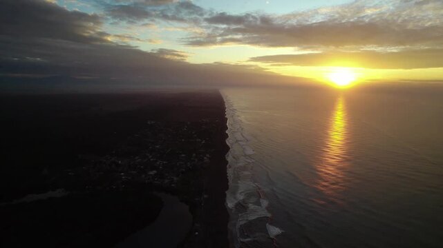 Drone zoom out capturing a wide view of the ocean at sunset in Los Cristianos, with gentle waves and warm golden light reflecting on the sea.