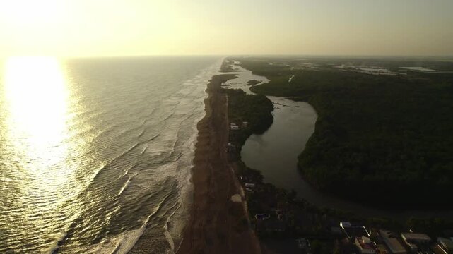Zoom in drone shot following the Atlantic coastline at sunset near Los Cristianos, Tenerife showing shoreline, waves and warm golden reflections.