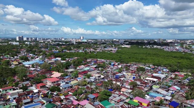 Aerial cityscape of Iloilo City Philippines showing expanding residential districts and tropical coastline under bright clouds. Dynamic urban growth and coastal development on Panay Island.