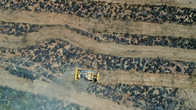 Heavy duty dozer clears brush in dry landscape, overhead aerial view