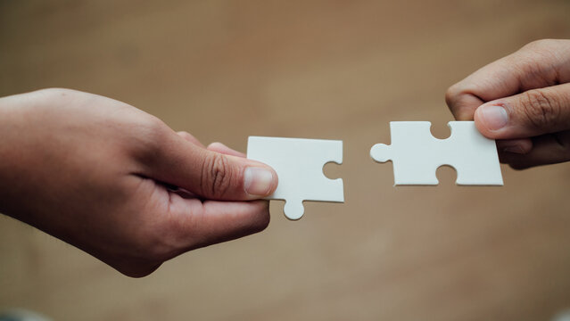 Close up of business hands joining white jigsaw puzzle pieces for teamwork and collaboration concept