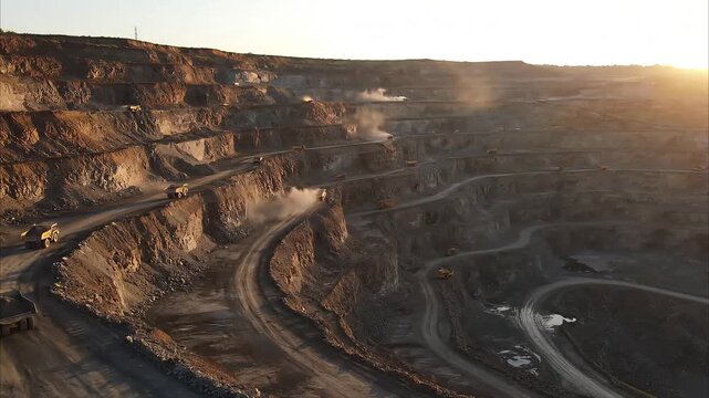 Large mining operation with trucks on winding roads at sunset