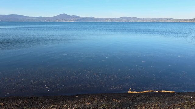 Calm blue waters of Bracciano volcanic lake on a sunny day in Anguillara Sabazia, Lazio region, Italy