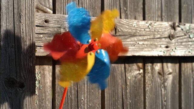 Colorful pinwheel spinning in the wind against a rustic wooden fence, symbolizing outdoor play and childhood fun