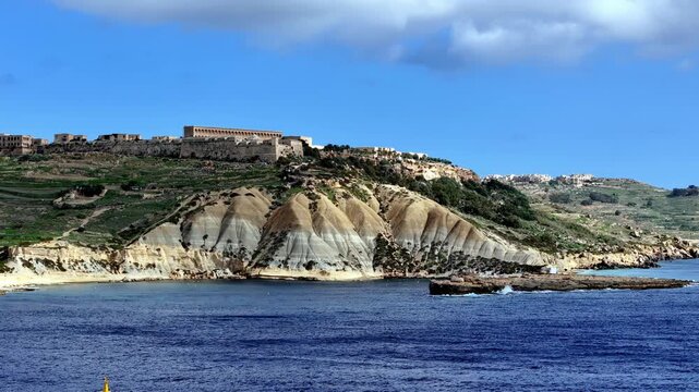 Fort Chambray Atop Striking Clay Slopes Overlooking Deep Blue Mediterranean Waters Under Sunny Skies During Vibrant Summer In Gozo Malta Capturing Scenic Coastal Cliffs From A Low Perspective