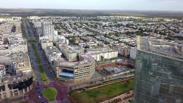 Detailed aerial drone shot of the top of Maroc Telecom skyscraper. Reveals technical antennas and rooftop engineering with a vast view of the Hay Riad business district in the background.