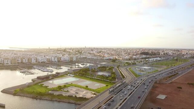 Aerial drone shot of the Rabat-Sal&eacute; tramway crossing the Hassan II bridge at sunset. Features busy traffic, the Bouregreg Marina, and urban coastline landscape in Morocco.