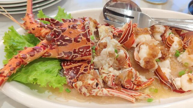 Video highlights a beautifully plated spiny lobster served on a bed of fresh green lettuce. The lobster is split open to reveal tender white meat, delicately garnished with savory sauce. Its vibrant o