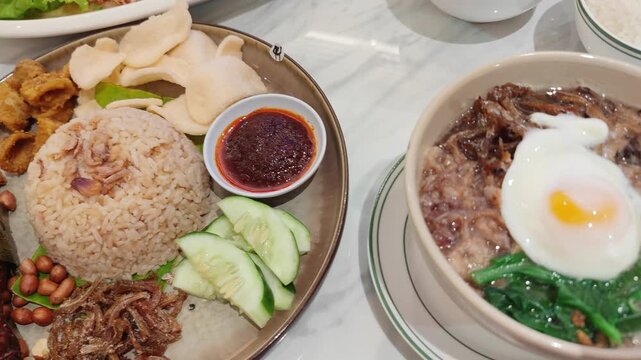 Video presents a beautifully arranged plate of Nasi Lemak, Malaysia&rsquo;s iconic national dish. A mound of fragrant coconut rice topped with fried shallots sits at the center, surrounded by sambal chili p