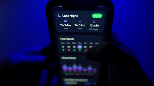 User holding a smartphone with an open mobile app for monitoring sleep quality in a dark room with blue backlight