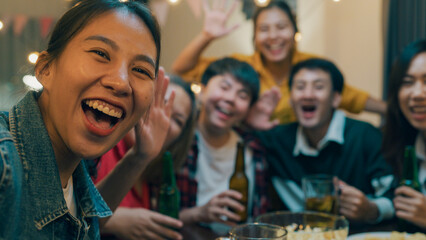 Closeup Group of diversity adult Asia people use phone greeting friend on remote video call hangout party at dining table in night life indoor home. Happy hour millennial generation inside house. © tirachard