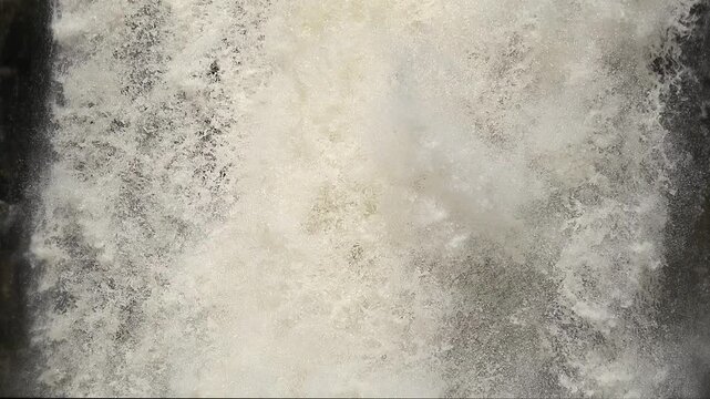 Waterfall droplets and spray erupt in powerful super slow motion, dense white turbulence. Cascade mist beads descend by gravity, showing frothy tan splash texture, close detail.