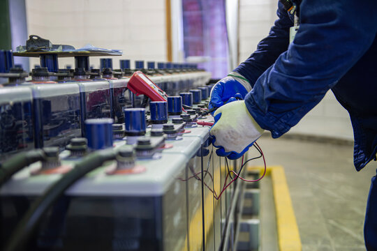 Technician performing voltage inspection on emergency battery bank and checking connections, as part of the maintenance of backup equipment