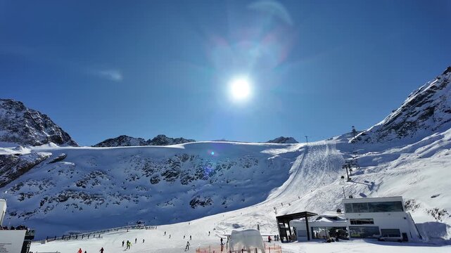Wide panoramic winter landscape of the ski resort in S&ouml;lden, Austria, captured under bright alpine sunshine. The image shows a high-altitude glacier slope in the &Ouml;tztal Alps with ski lifts, groomed pi