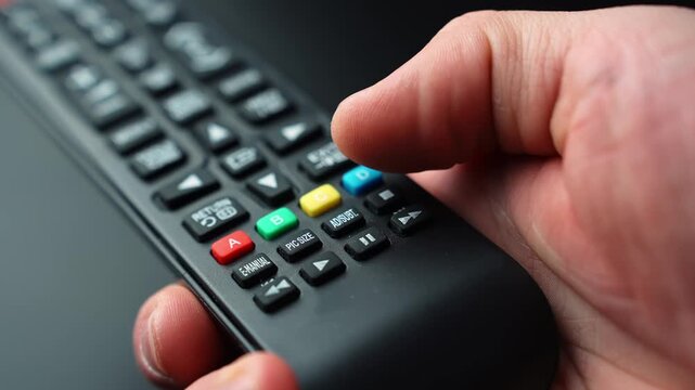Close-up of a hand pressing the rewind button on a TV remote control, skipping back during video playback with shallow depth of field for streaming and home entertainment b-roll.