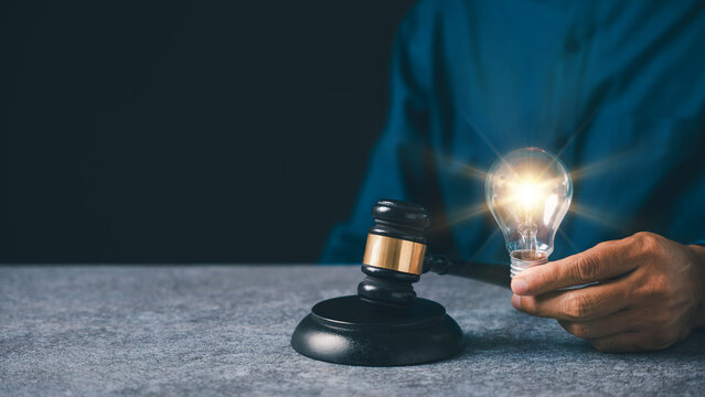 Intellectual property patent law protects light bulb idea concept, hand holds glowing lamp near judge gavel for legal business innovation and corporate asset protection