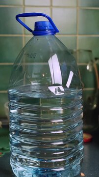 Large plastic jug with handle and blue cap on a kitchen counter, filled with clear drinking liquid. Everyday hydration, household storage, and emergency supply concept.