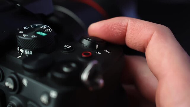 Close-up hand flips the power switch to ON on a mirrorless camera top plate, with mode dial and soft studio bokeh&mdash;ideal for creator gear and tech b-roll.