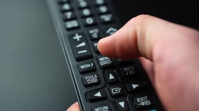 Close-up of a hand pressing the MENU button on a TV remote control, opening settings and on-screen options with shallow depth of field for home entertainment tech b-roll.