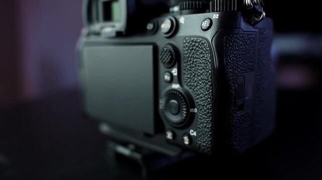 Close-up of mirrorless interchangeable-lens camera body with flip-out LCD screen and control dials in moody studio lighting, shallow depth of field.